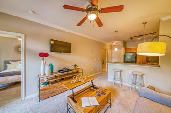 A living room with a ceiling fan and a flat screen TV mounted on the wall.